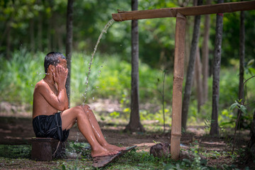little boy bathing outdoor from a traditional bamboo chute,countryside Thailand.