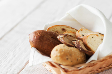 Fresh bread assortment on white wooden background, copyspace. Warm baked sweet products, served in rustic basket