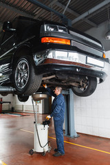 Change engine oil and transmission inspection in SUV. Car on the lift in garage, working mechanic under vehicle