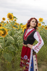 Obraz na płótnie Canvas Girl in a traditional Bulgarian dress feeling happy in a field of sunflowers