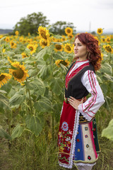 Fototapeta na wymiar Girl in a traditional Bulgarian dress feeling happy in a field of sunflowers