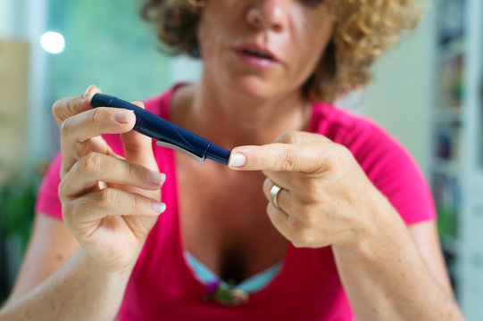 Close up of a female diabetic patient using lancelet on finger to take sample of blood sugar.