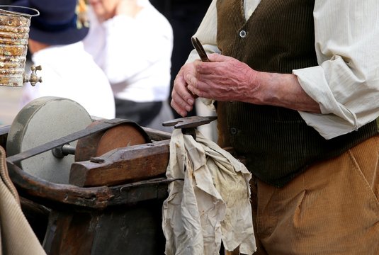 Senior while sharpens knife in old grindstone