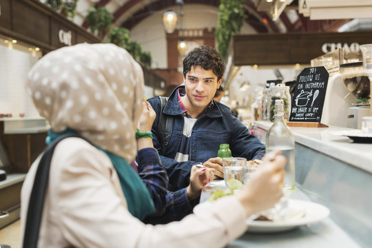 Man looking at female friends while having food in railroad station cafe