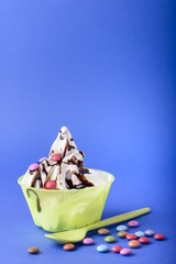 frozen yogurt with chocolate and chocolate candy topping on blue background with green spoon and chocolate candy