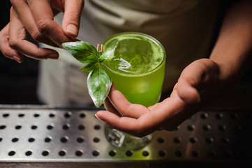 Barman is decorating cocktail with basil