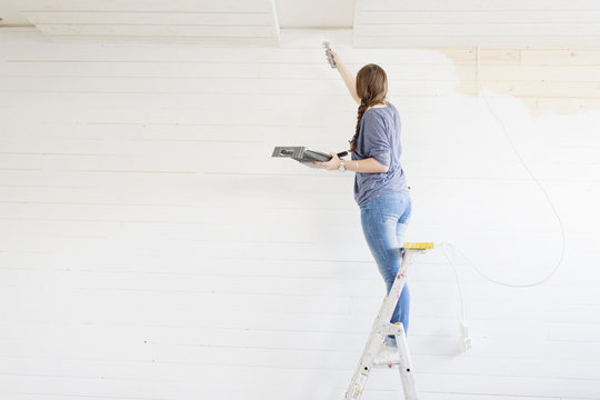 Rear view of woman painting wall with paint brush