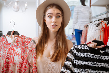 Confused woman choosing dress in clothing store