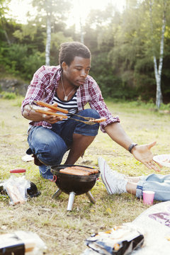 Young man serving grilled sausage in plate during picnic