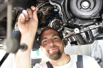 freundlicher Automechaniker repariert Motor eines Fahrzeuges in der Werkstatt // friendly car mechanic repairs engine of a vehicle in the garage