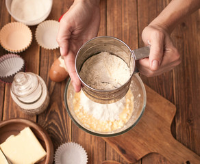 Woman hands, ingredients and devices for preparation muffin on a wooden background. House pastries. Food concept. Flour, eggs, butter, mix for pastries. 