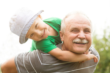 the grandfather plays with the grandson on shoulders in park

