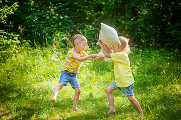 Obraz premium Children fighting together with pillows in a sunny summer garden