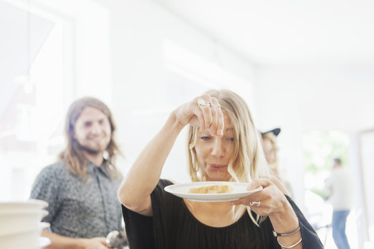 Playful woman sprinkling salt on bread with man standing in background at restaurant