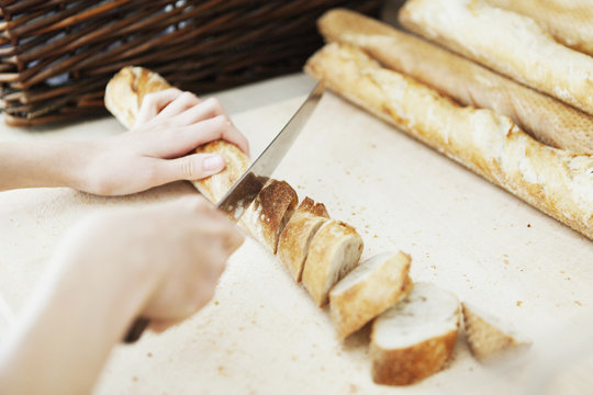 Cropped image of chef's hands cutting breadstick on table