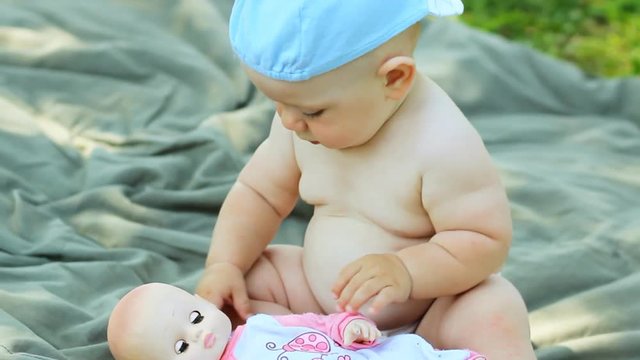 Charming Baby Boy Playing In The Garden With A Small Doll And Stroller