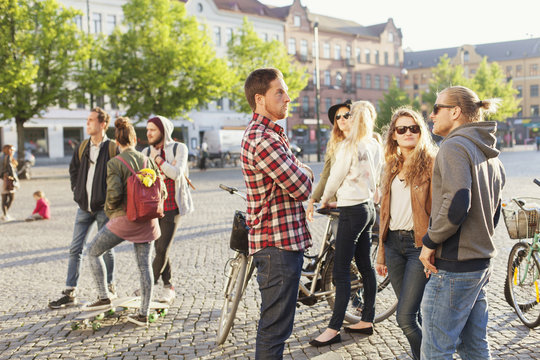 Group of friends with bicycles and skateboards standing on city street