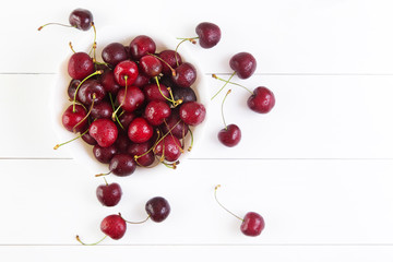 Obraz na płótnie Canvas Ripe red cherries with water drops in bowl on a white background. Top view with copyspace