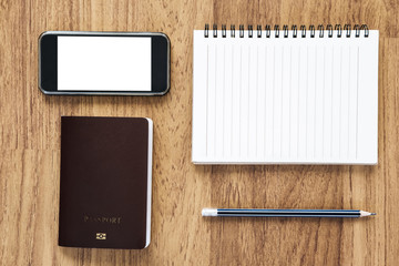 Blank notebook and mobile phone with passport on wooden desk, travel concepts