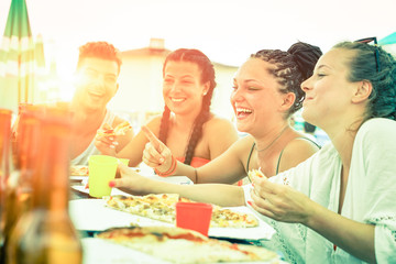 Friends having fun eating pizza at sunset on beach bar restaurant - Cheerful teenagers laughing at dinner party on summer vacation - Concept of joyful meal together