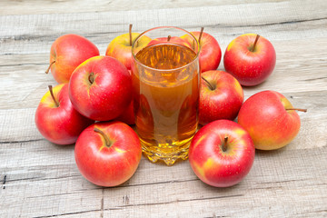 glass of juice and ripe apples on a wooden background