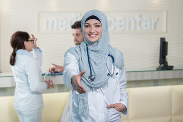 Obraz premium Young happy smiling female muslim doctor giving hand for handshaking.