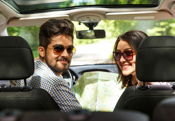 Happy young couple with a map in the car. They are using map on road trip.