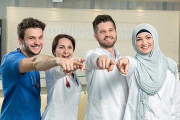 Obraz premium healthcare and medicine concept - attractive male doctor in front of medical group in hospital showing thumbs up