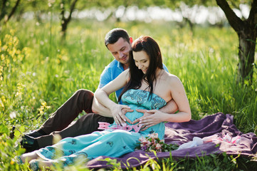 Happy pregnant couple at turquoise dress on the garden