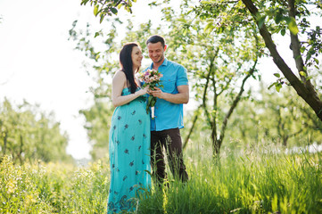 Happy pregnant couple at turquoise dress on the garden