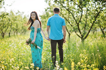 Naklejka na ściany i meble Happy pregnant couple at turquoise dress on the garden