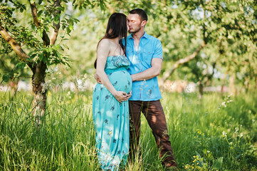 Happy pregnant couple at turquoise dress on the garden