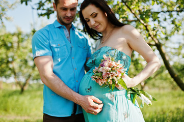 Happy pregnant couple at turquoise dress on the garden