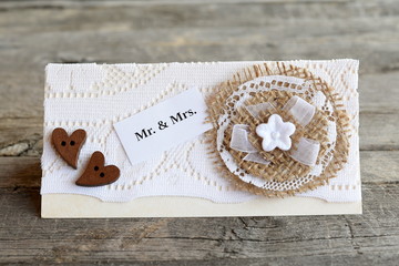 Beautiful wedding invitation on old wooden background. Handmade wedding invitation card decorated with lace and burlap flower and wooden buttons hearts. Vintage card diy