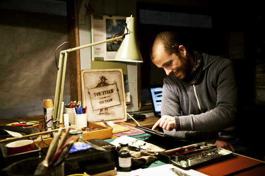 A man in his workshop using a digital tablet with a touch screen surrounded by equipment for signwriting and screen-printing. 