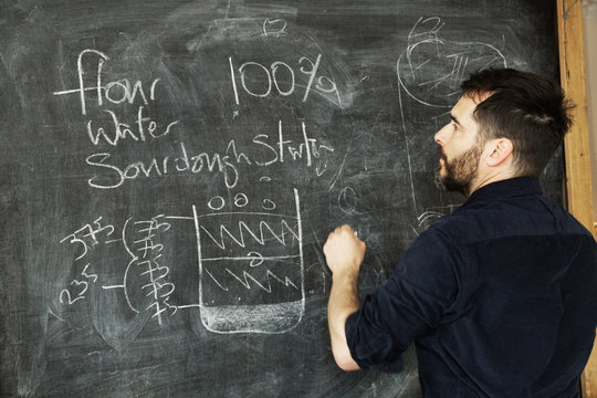 Baker standing in front of a blackboard, writing a recipe for bread.