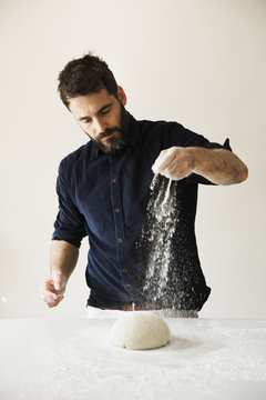 Baker standing at a table, liberally sprinkling flour over bread dough.