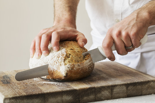 Close up of a baker slicing a freshly baked loaf of bread with a bread knife.