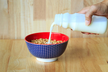 Someone pour milk in the bowl of cereals.
