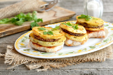 Roasted Turkey fillet with potatoes, zucchini and parsley on a plate and on a burlap. Fork and knife on a cutting board, fresh parsley, salt shaker on old wooden table. Delicious lunch or dinner idea