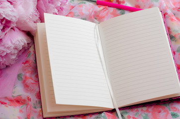 Open pink notebook on a beautiful pink background. Flowers near the notepad