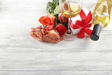 Bottle of wine, gift boxes and roses on a wooden background