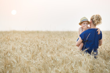 Woman with adorable little child walking in the wheat field. Mother with cute toddler boy. Motherhood and lifestyle concept.