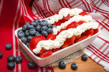 Whip Cream, strawberries and blueberries combined to look like the american flag and placed in a ceramic tray  for a 4th of july themed party, on a wooden table and rustic towel