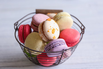 Colorful tasty macaroons in metallic bowl on light background