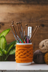 Jar with knitted cover holding different sized knitting needles and crochet hooks.