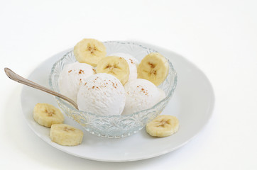 Vanilleeis und Banane   / Vanilleeis mit Bananen Scheiben in einer Glasschale auf einem weißen Teller, Nahaufnahme, Makro, weißer Hintergrund, Textfreiraum, Freiraum für Text, horizontal
