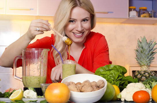 Happy gorgeous, healthy woman putting honey in freshly made smoothie