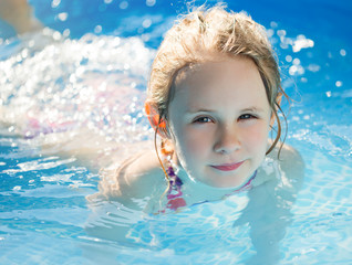 Fototapeta na wymiar Portrait of cute little girl in blue big inflatable pool outdoors