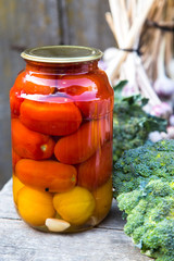 tinned tomatoes are in a glass on the gray wooden table and broccoli and garlic as background